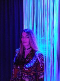 Young woman looking away while standing against blue curtain