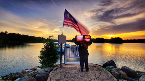 Flag by lake against sky during sunset