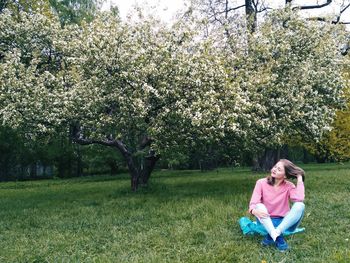 Woman sitting on branch with fresh pink flowers in park