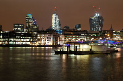 Illuminated buildings by river against sky in city at night