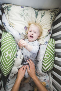 Crying baby boy lying in crib while hands of father reaching for him