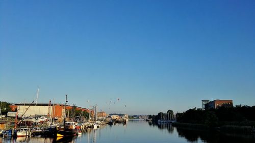 Boats moored at harbor against clear blue sky