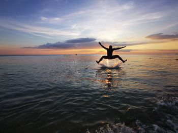 Silhouette person in sea against sky during sunset