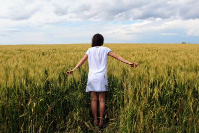 Rear view of woman standing in field against sky