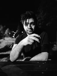 Portrait of young man sitting by table against sky at night