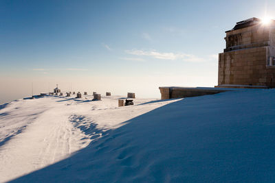 Snow covered land by sea against sky