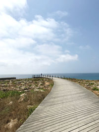 Boardwalk leading towards sea against sky