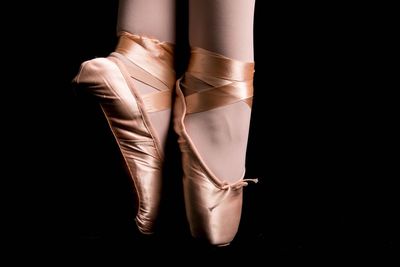 Low section of ballet dancer dancing against black background