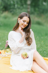 A happy smiling girl holds an apple in her hands and sits on a yellow blanket at a summer picnic