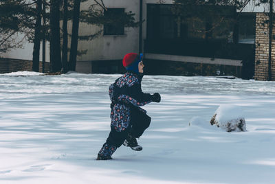 Side view of boy running on snow covered field