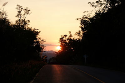 Road amidst trees against sky during sunset