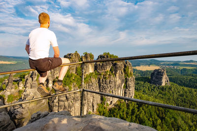 Young ginger hiker sit on handrail at mountain peak with stairs, during sunrise foggy morning