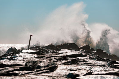 Waves breaking on rocks against sky