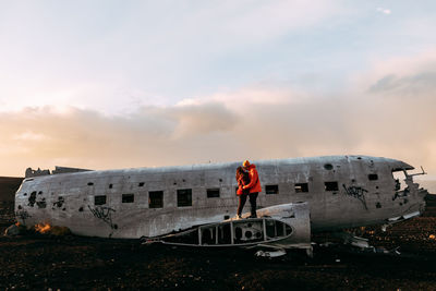 Rear view of man standing on abandoned airplane against sky during sunset