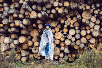 Woman director is standing by a log at a sawmill in a scarf and a blue hat in autumn