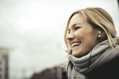 Side view of cheerful businesswoman wearing earphones against sky