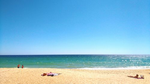 People on beach against clear blue sky