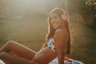 Portrait of beautiful woman wearing bikini listening music while sitting on blanket