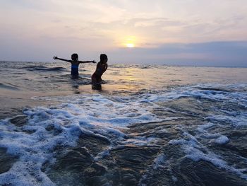 People in sea against sky during sunset