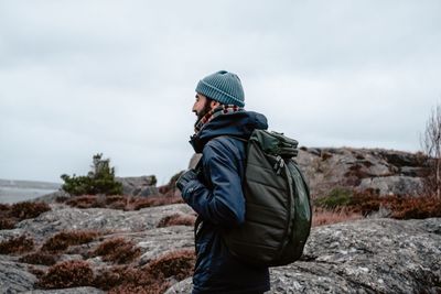 Side view of male hiker with backpack standing against sky