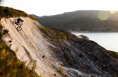 Young man riding bicycle on mountain against clear sky