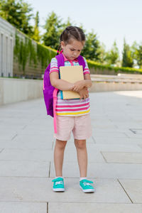 Girl with books and backpack standing on footpath