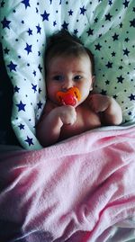 High angle view of cute baby girl with pacifier lying on bed at home