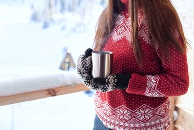 Midsection of woman wearing sweater holding coffee cup in winter
