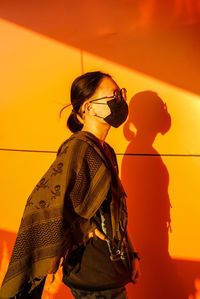 Side view of woman standing against yellow wall