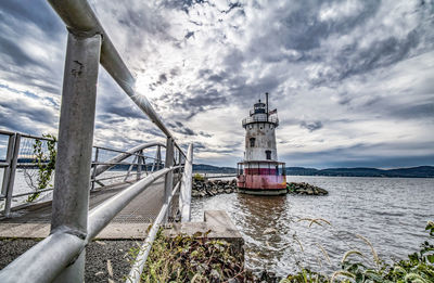 Lighthouse amidst buildings and sea against sky