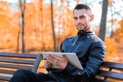 Portrait of young man using mobile phone while sitting on seat