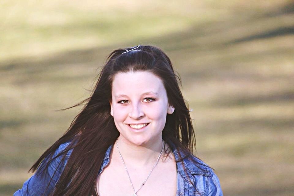 headshot, portrait, looking at camera, person, young adult, focus on foreground, front view, lifestyles, long hair, young women, close-up, smiling, leisure activity, head and shoulders, brown hair, contemplation, black hair