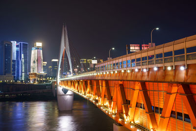 Illuminated bridge over river by buildings in city at night