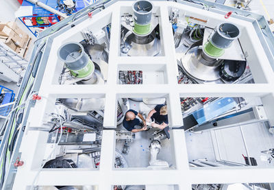 Top view of two colleagues working at industrial robot in modern factory