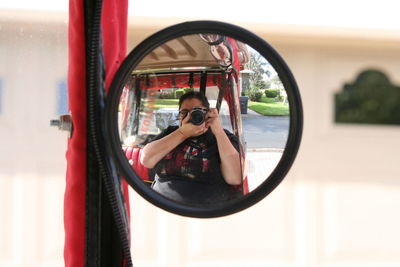 Woman photographing while reflecting in vehicle mirror