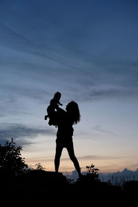 Silhouette man with woman standing against sky during sunset