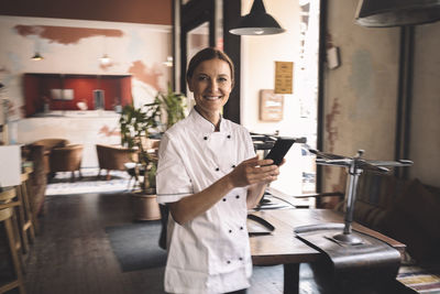 Portrait of smiling chef with smart phone in restaurant