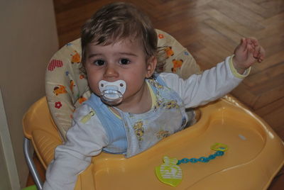 Portrait of cute baby boy sucking pacifier in walker at home