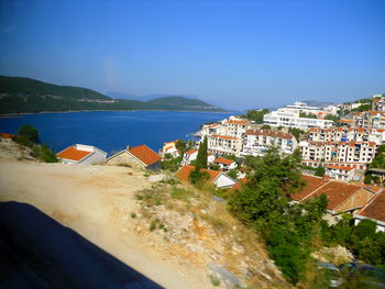 High angle view of townscape by sea against clear blue sky