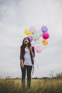 Full length of woman with balloons standing on field against sky