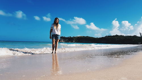 Full length of woman standing on shore at beach against blue sky