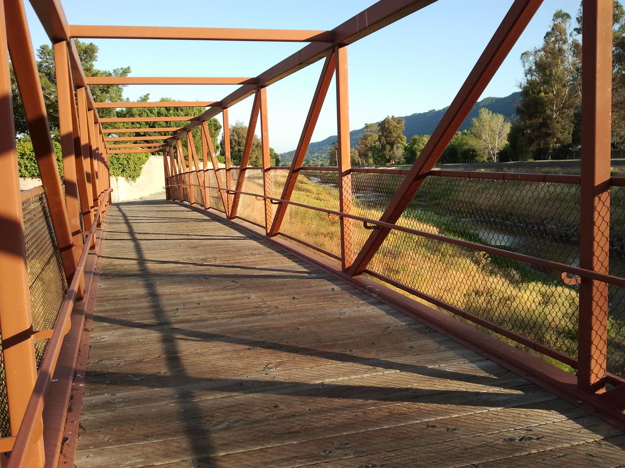 the way forward, built structure, railing, architecture, transportation, metal, diminishing perspective, bridge - man made structure, connection, clear sky, sunlight, shadow, tree, railroad track, vanishing point, footbridge, day, sky, outdoors, fence