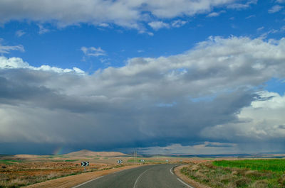 Empty road amidst field against sky