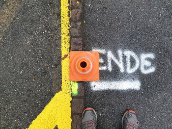 Worn sneakers in front of the traffic cone next to the road boundary. 