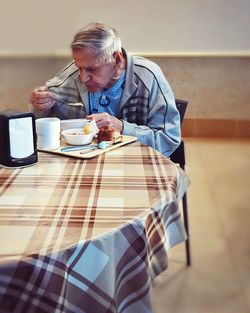 Senior man eating food while sitting at table in hospital