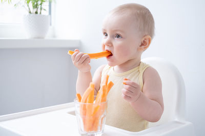 Boy eating carrot sitting on high chair at home