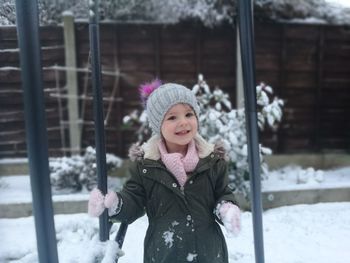 Portrait of smiling girl standing by swing during winter