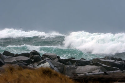 Waves splashing on rocks at beach against sky