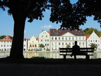 Silhouette people sitting on bench by footpath against buildings in city