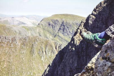 Low section of hiker sitting on mountain during sunny day